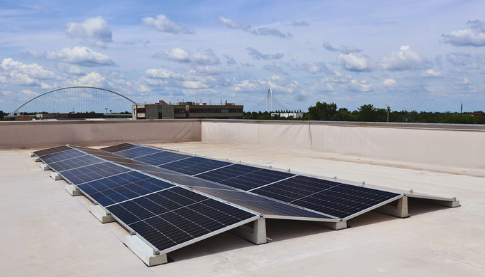 Auf einem Flachdach installierte Solarmodule mit einer Stadtlandschaft und einem teilweise bewölkten Himmel im Hintergrund. - © Basic