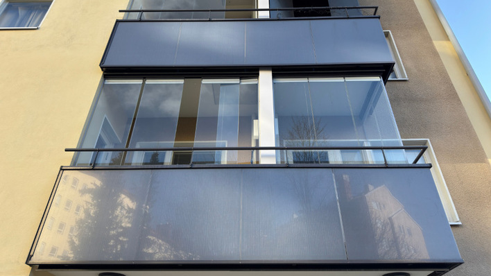Ein modernes Wohnhaus mit Glasbalkonen, in denen sich der Himmel und die umliegenden Gebäude spiegeln. - © Lumon Deutschland